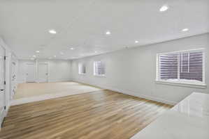 Spacious room featuring wood-finish flooring and neutral carpet, white walls, multiple recessed lights, and several white doors with black hardware