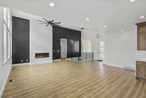Vaulted ceiling great room featuring a linear electric fireplace, wood-finish flooring, a contemporary ceiling fan, and tall windows
