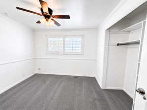 Unfurnished bedroom featuring dark carpet, crown molding, a closet, and a ceiling fan