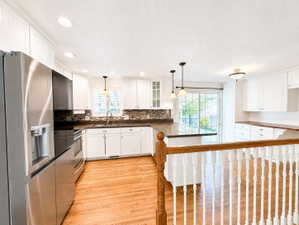 Kitchen featuring stainless steel appliances, white cabinets, light wood-type flooring, and glass fronted cabinets