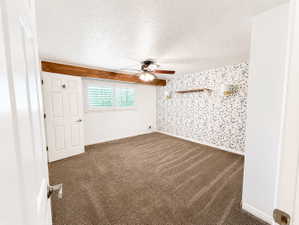 Unfurnished room featuring  dark carpet, a textured ceiling, ceiling fan, and an accent wall