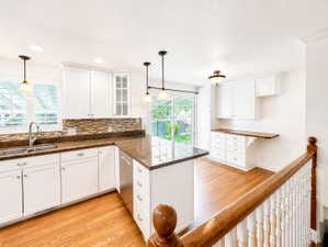 Kitchen with white cabinetry, light wood finished floors, a peninsula, glass insert cabinets, and decorative backsplash