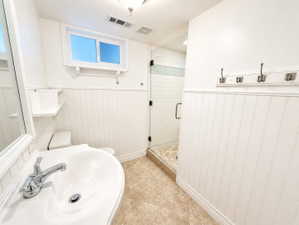 Bathroom with a shower stall, light tile patterned floors, and wainscoting