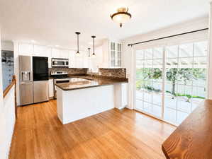 Kitchen with dark stone counters, stainless steel appliances, a peninsula, white cabinetry, and light wood-style flooring