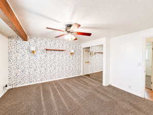 Unfurnished room with carpet, a textured ceiling, beam, ceiling fan, and wallpapered wall