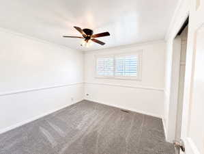 Unfurnished bedroom featuring dark carpet, a ceiling fan, ornamental molding, and a closet