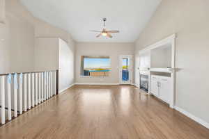 Unfurnished living room with lofted ceiling, a ceiling fan, light wood-type flooring, and a glass covered fireplace