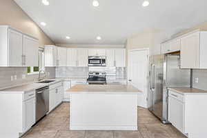 Kitchen with backsplash, stainless steel appliances, a kitchen island, white cabinetry, and lofted ceiling