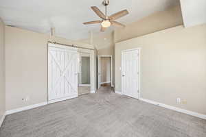 Unfurnished bedroom with a barn door, light colored carpet, a ceiling fan, vaulted ceiling, and ensuite bath
