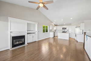 Unfurnished living room featuring light wood finished floors, vaulted ceiling, a ceiling fan, a fireplace with flush hearth, and recessed lighting