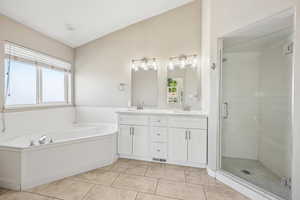 Full bath with double vanity, a shower stall, light tile patterned flooring, a garden tub, and lofted ceiling