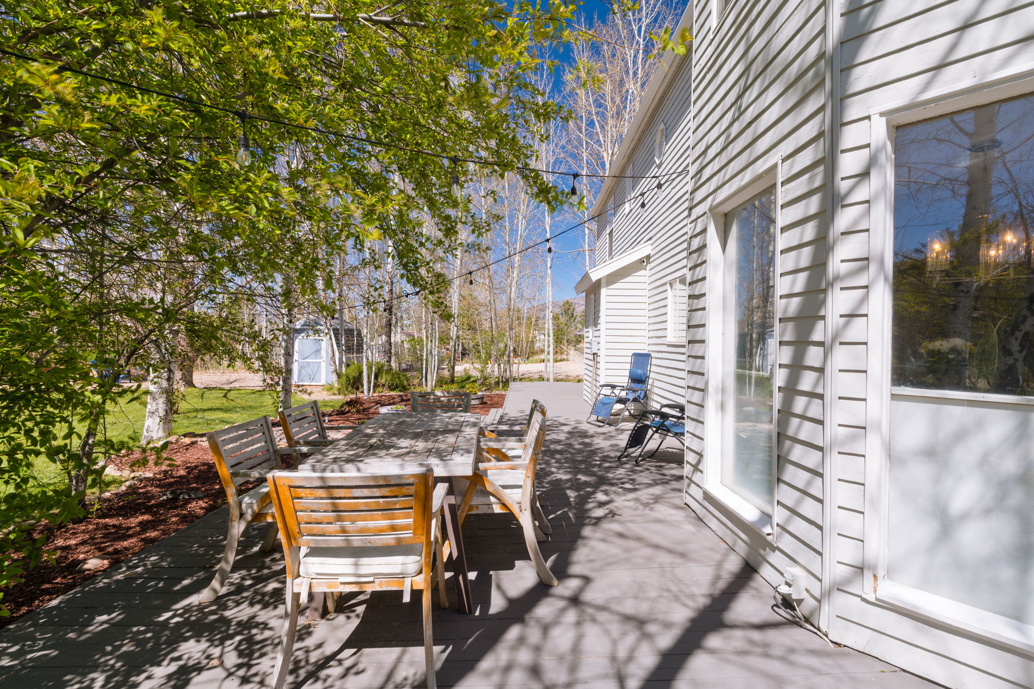 Expansive outdoor patio featuring a gray deck surface, string lighting, and mature trees providing natural shade