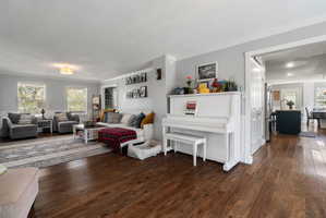 Open-concept living area featuring rich wood-finish flooring, a neutral wall palette, and crown molding
