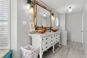 Bathroom featuring a double vanity with vessel sinks, ornate mirror, and wood-finish flooring