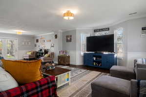Spacious living area featuring wood-finish flooring, white wainscoting, and crown molding