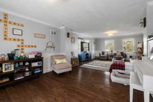Spacious living area featuring wood-finish flooring, light gray wall paint, white crown molding, and wainscoting