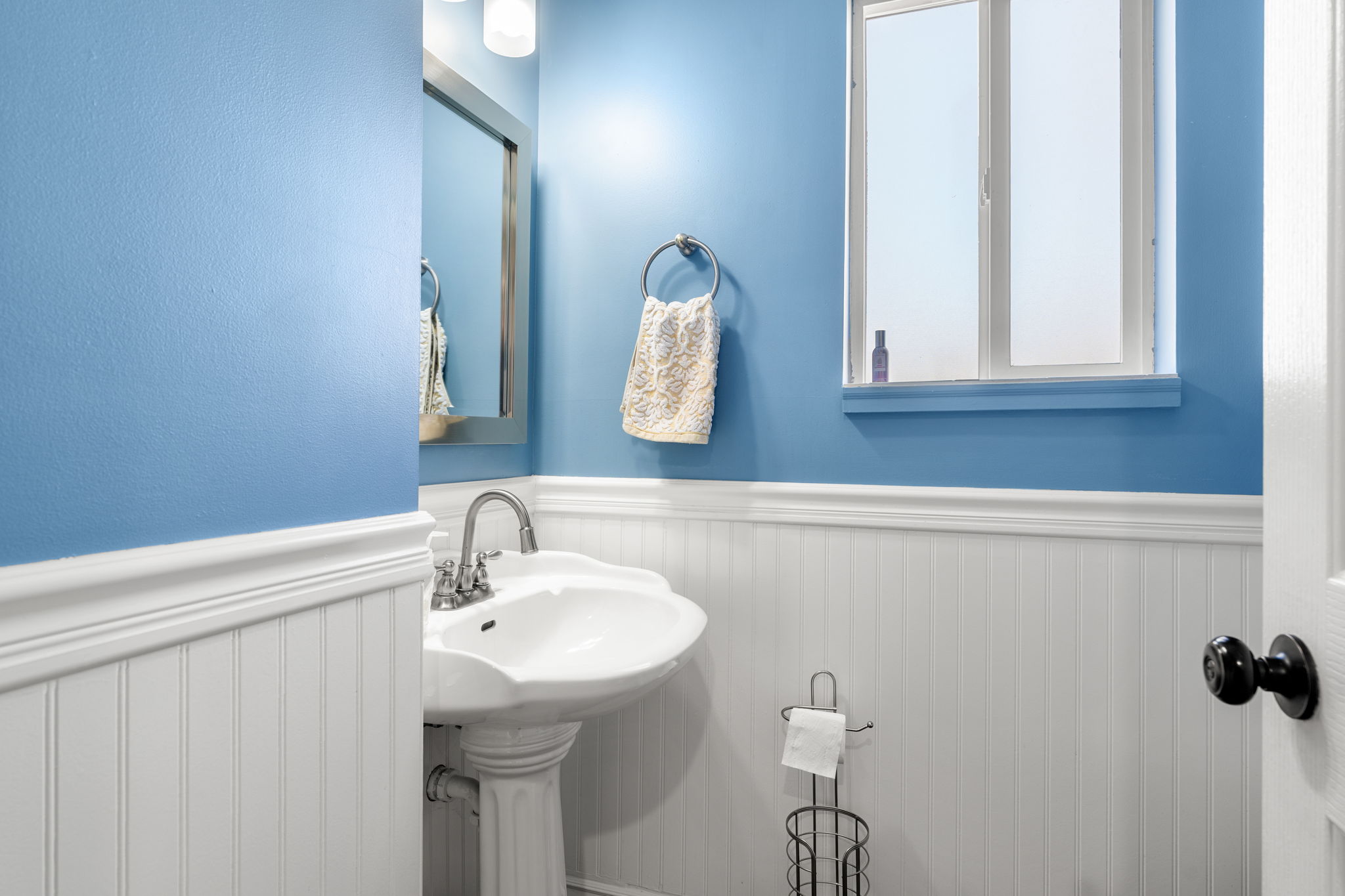 Pedestal sink with chrome faucet, complemented by white wainscoting and blue walls