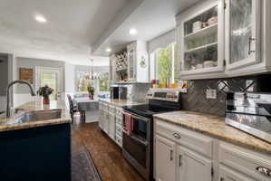 Kitchen featuring a stainless steel sink, granite countertops, white cabinetry with glass-front uppers, a herringbone tile backsplash, and wood-finish flooring
