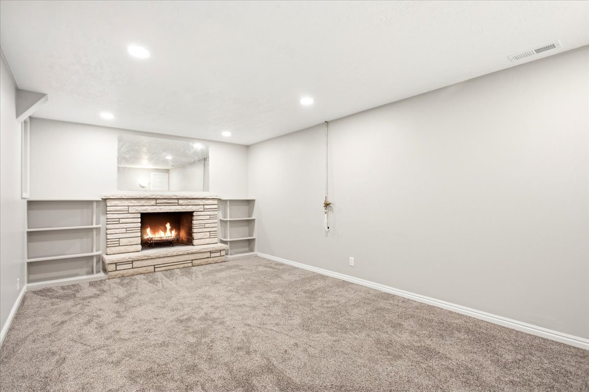Stone-clad fireplace with a hearth and built-in shelving, complemented by recessed lighting and wall-to-wall carpeting