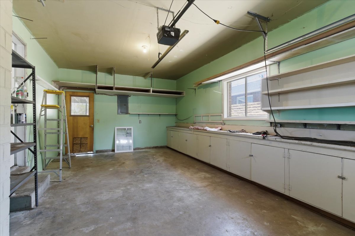 Spacious garage featuring a concrete floor, built-in lower cabinetry, a window offering natural light, an overhead garage door opener, and wall-mounted shelving