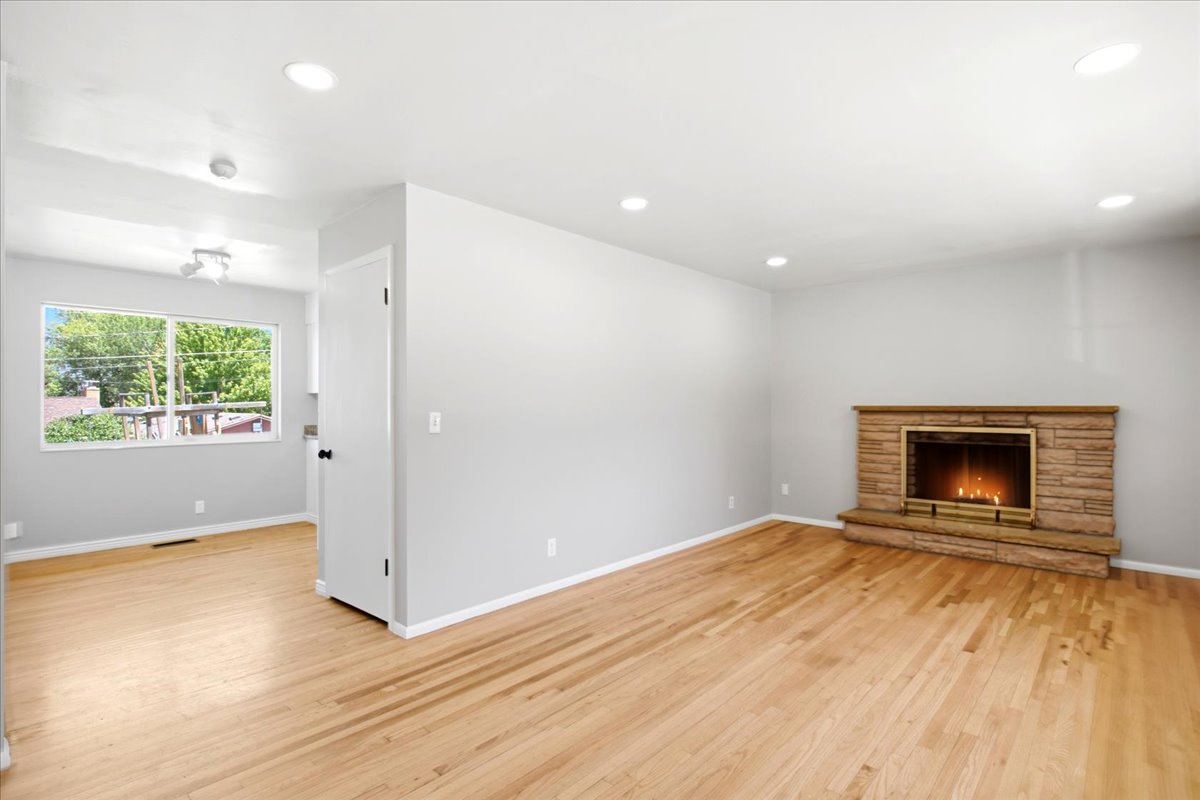 Spacious living area featuring wood-finish flooring, a stone-clad fireplace with a brass firebox, and recessed lighting