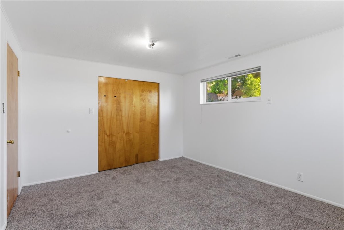 Room featuring gray carpet flooring, white painted walls, a horizontal window, and wood-finish bi-fold closet doors