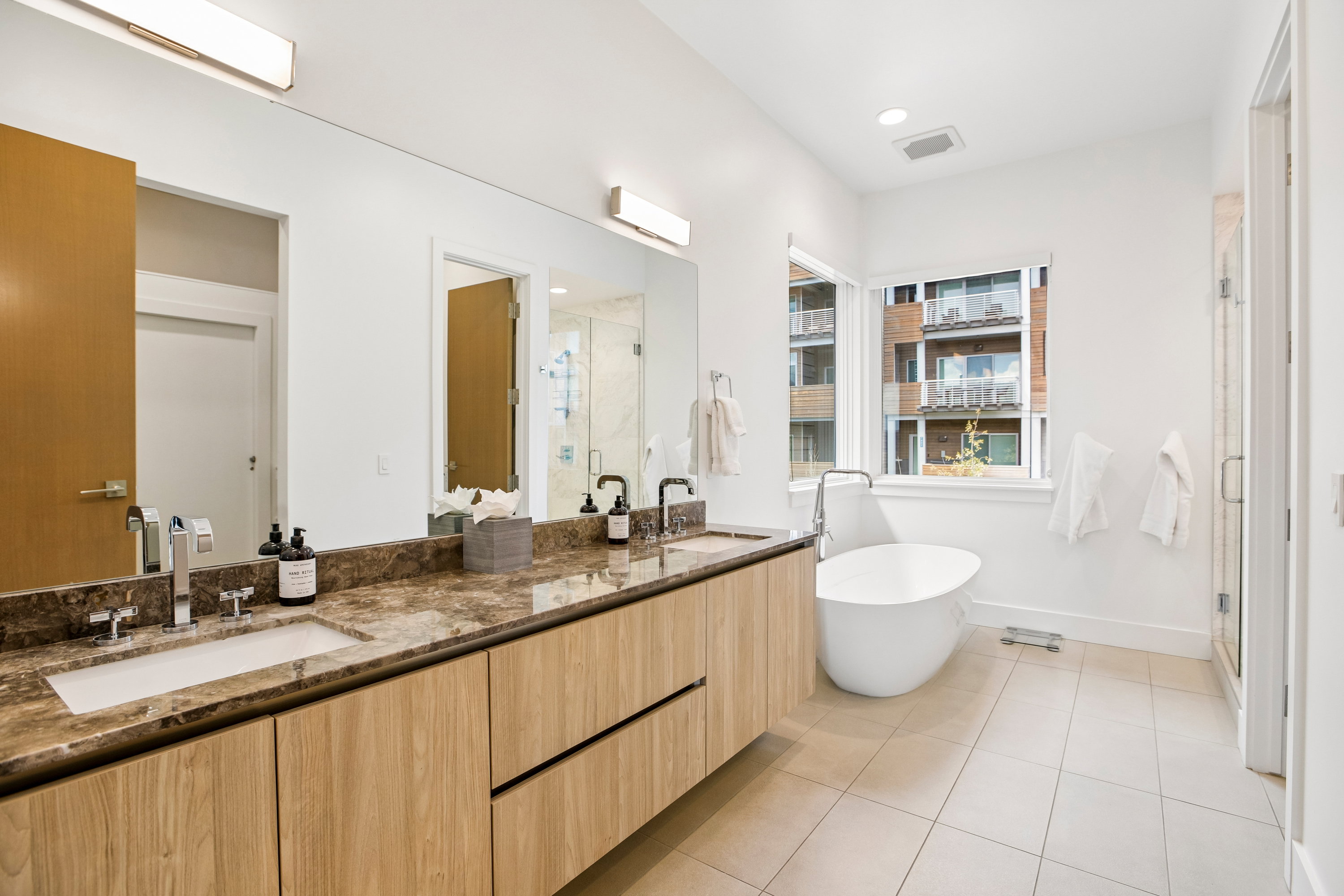 Contemporary bathroom featuring a freestanding soaking tub, dual vanity with undermount sinks, stone countertop, and a glass-enclosed shower