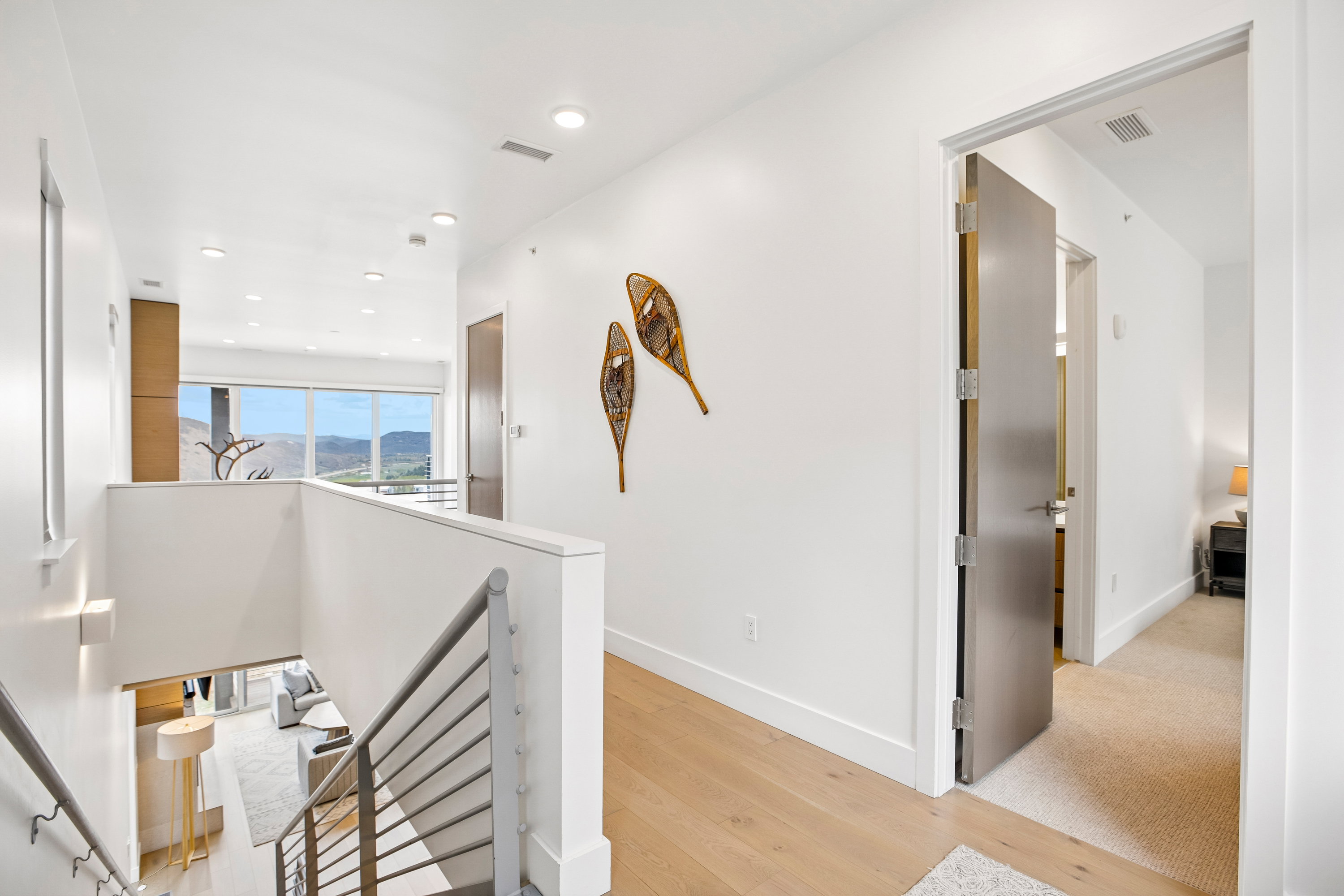 Upper-level hallway featuring light wood-finish flooring, recessed lighting, and a metal-railed staircase