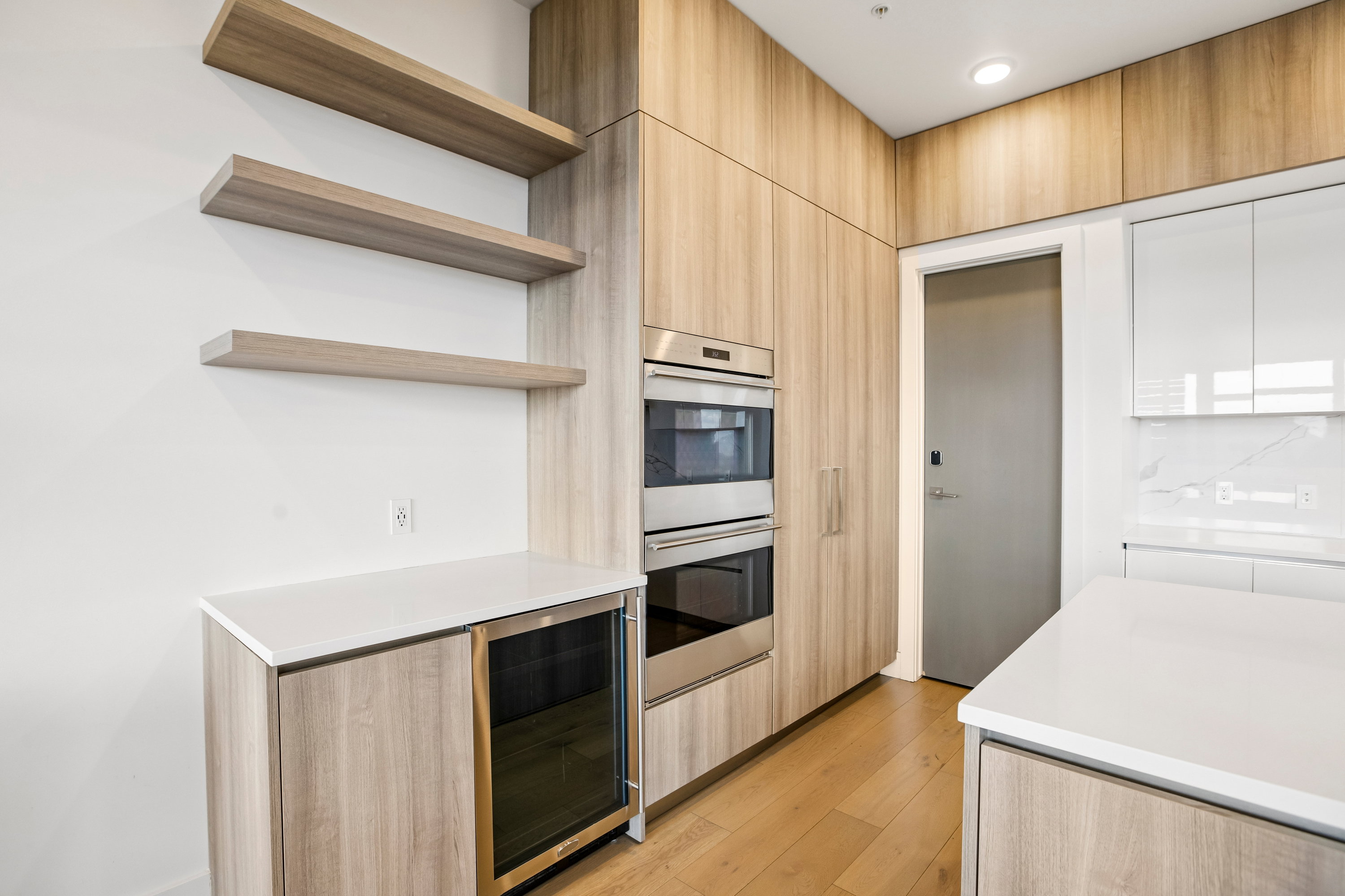 Modern kitchen featuring wood-finish cabinetry, integrated stainless steel double ovens, and a beverage cooler