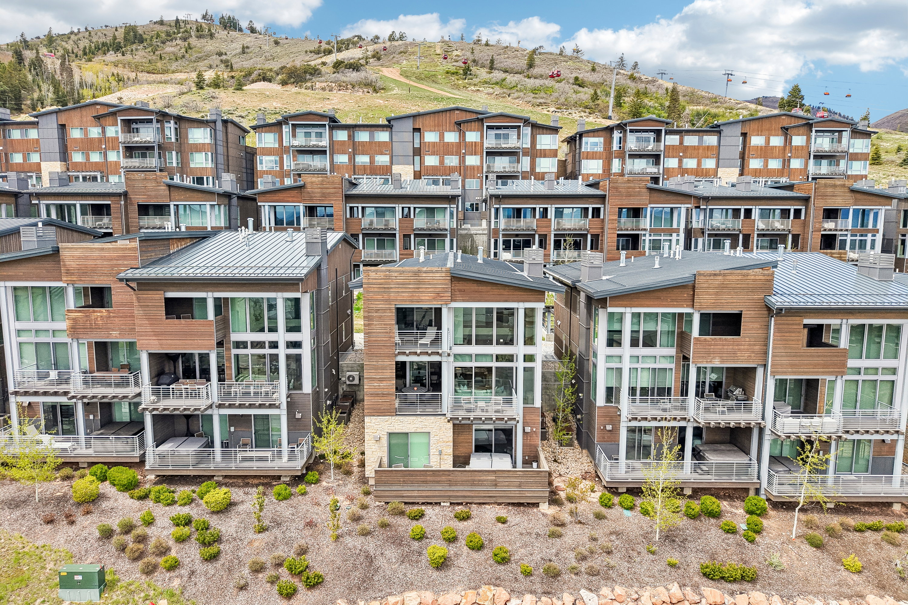 Contemporary multi-level exterior residences featuring wood paneling, extensive glass facades, multiple private balconies, ground-level patios, and integrated hot tubs