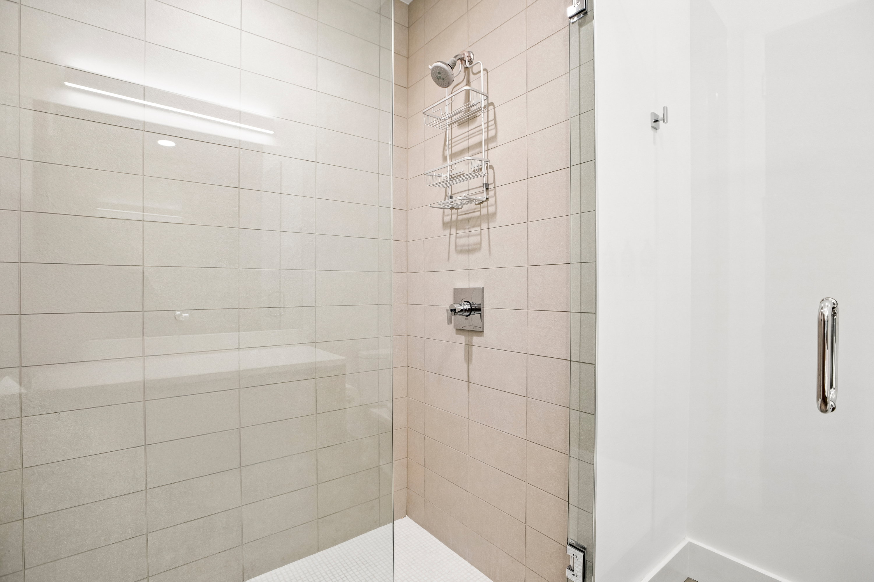 Shower enclosure featuring a frameless glass door, light-toned horizontal tile, a built-in shower bench, and a tiled shower pan