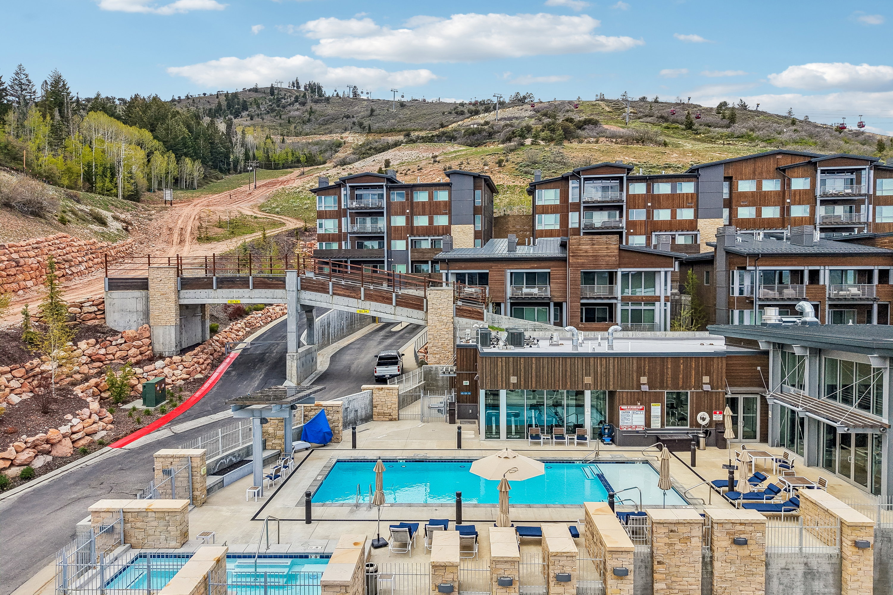Resort-style property featuring multiple pools, expansive outdoor lounging areas, a covered walkway, and multi-story buildings with private balconies