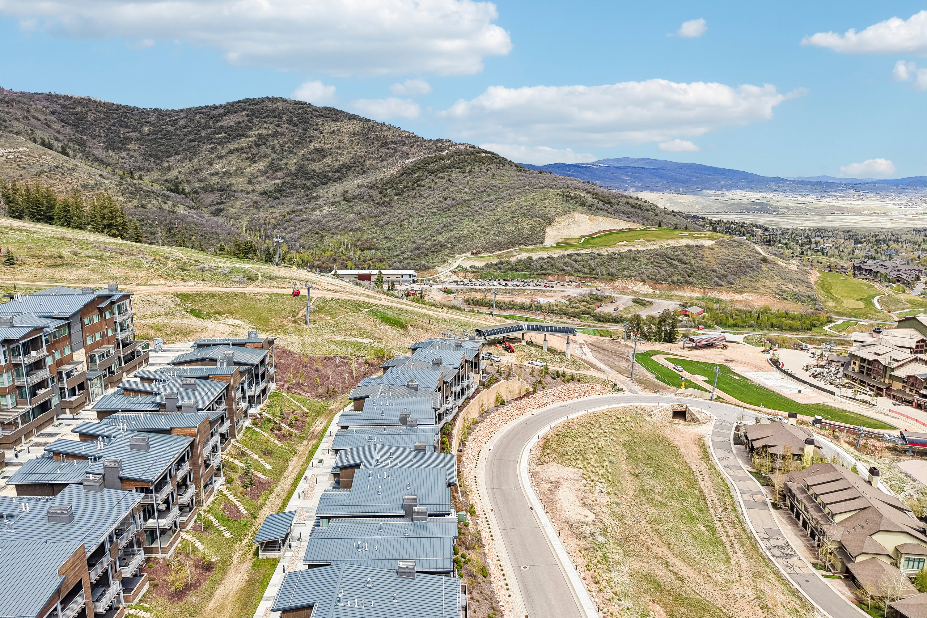 Modern multi-story buildings featuring balconies and dark grey roofs set against a mountainous backdrop