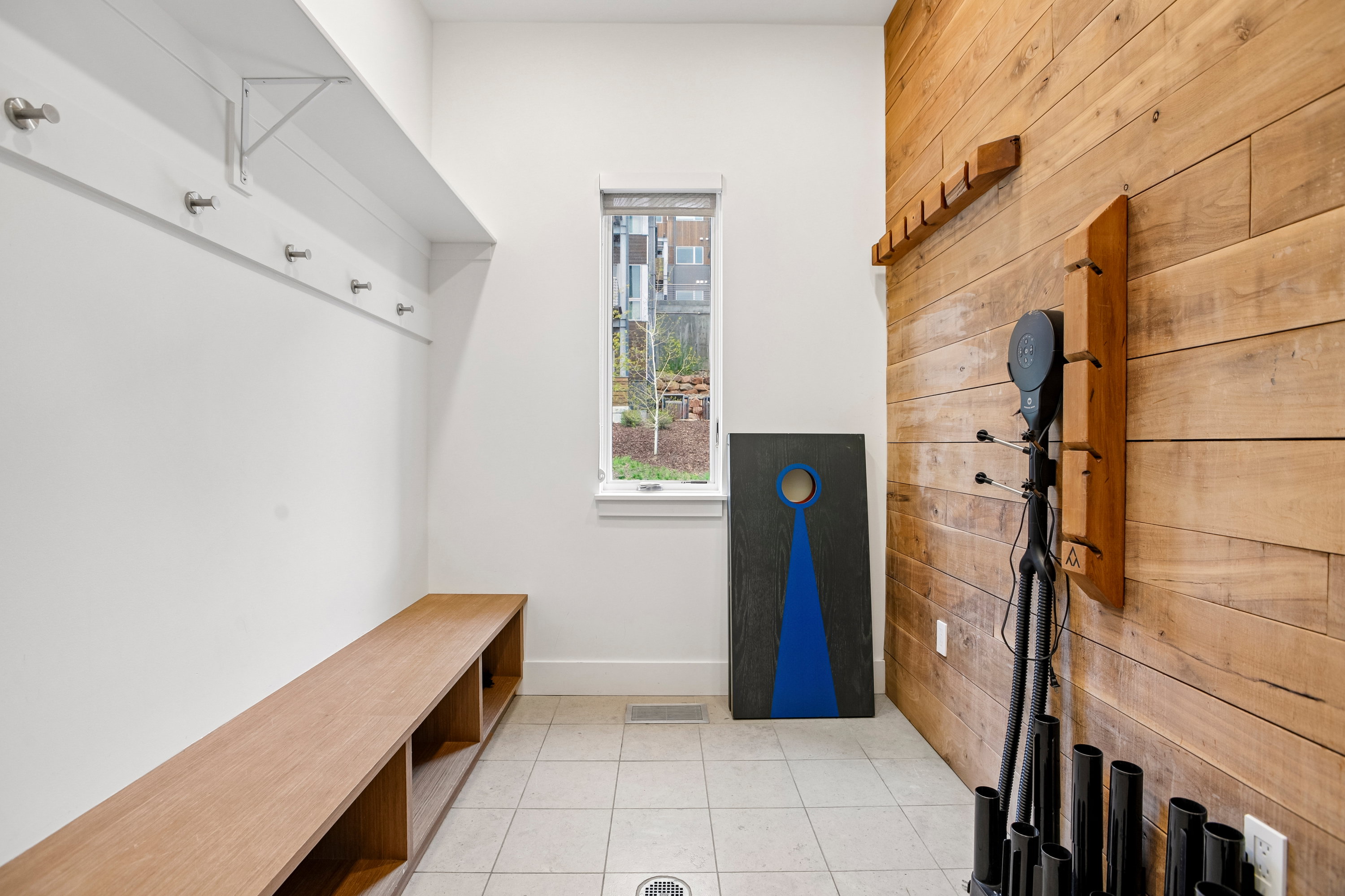 Entryway featuring a built-in wooden bench with open storage, a white wall-mounted shelf with coat hooks, and a contrasting wood-paneled accent wall