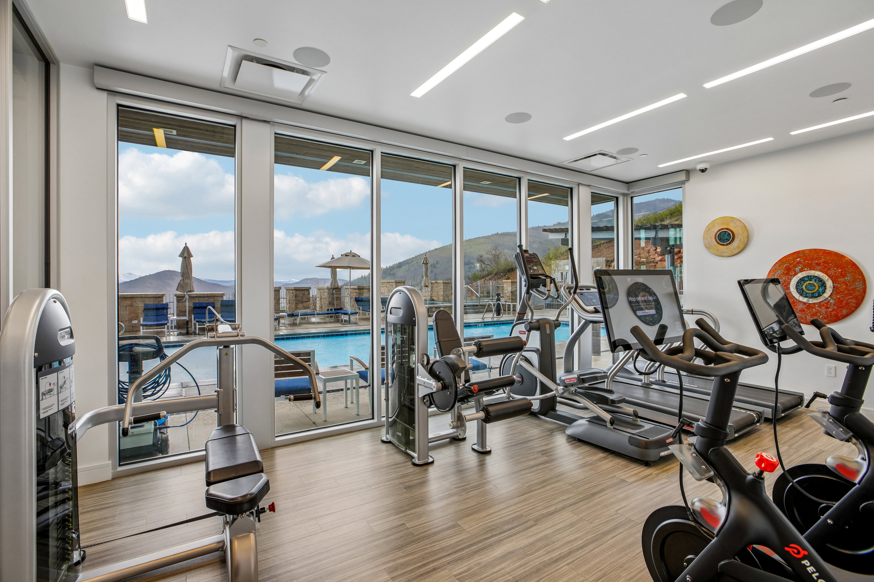 Fitness center with wood-finish flooring, ample natural light from floor-to-ceiling windows, and recessed ceiling lighting