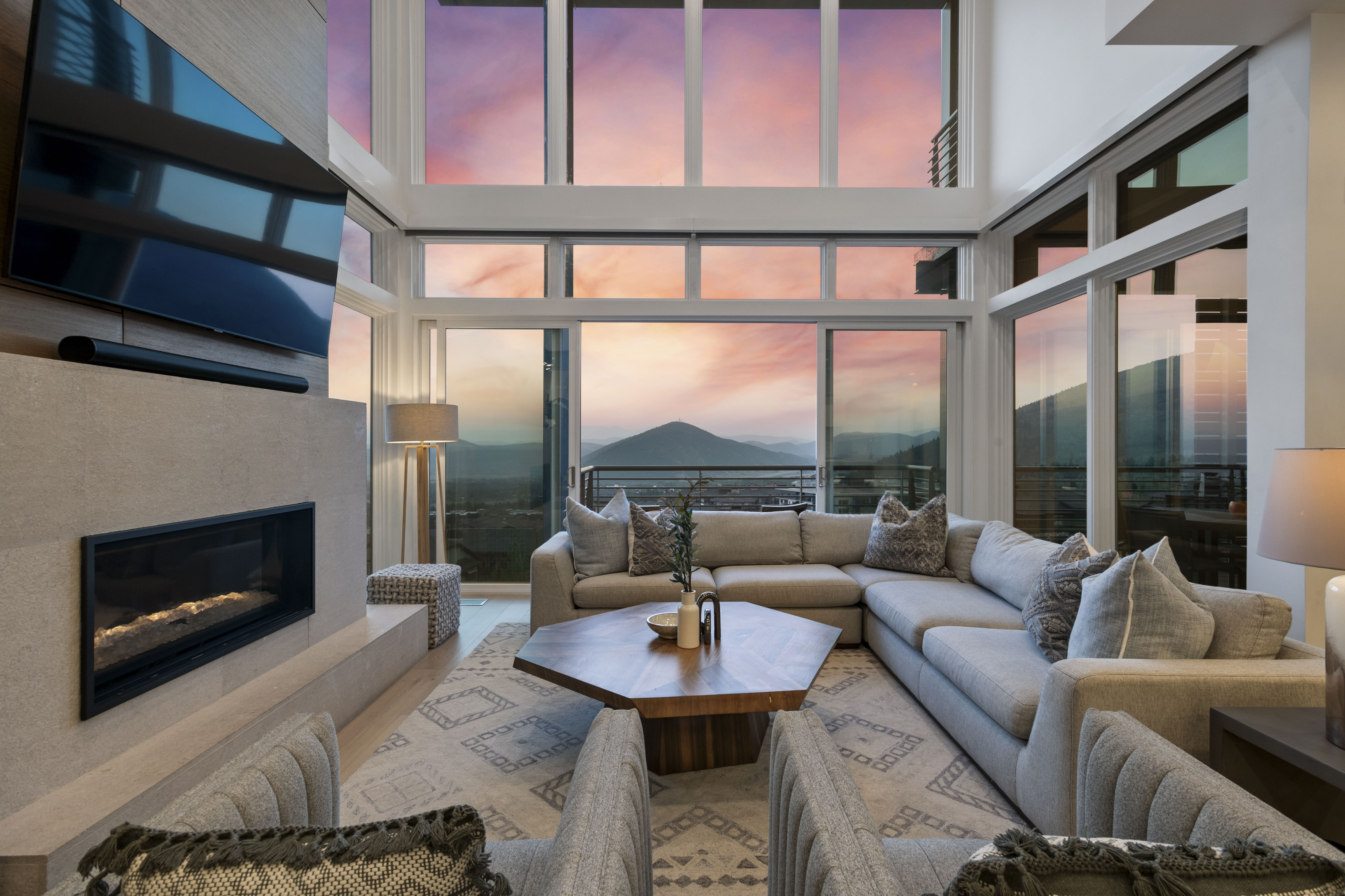 Living area featuring a floor-to-ceiling window wall, a linear fireplace with a textured surround, light-tone wood-finish flooring, and a mountain backdrop