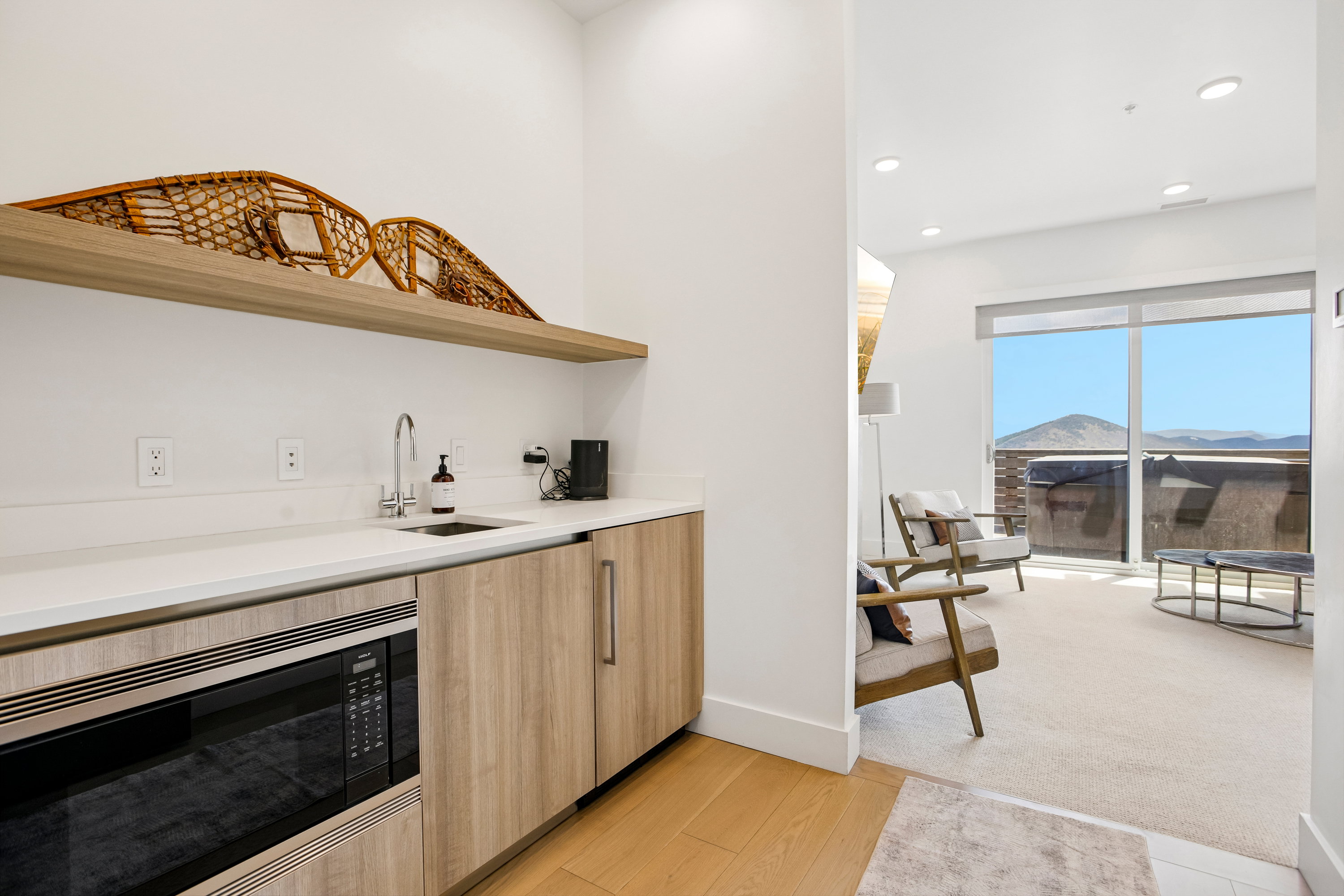 Contemporary wet bar with light wood-finish cabinetry, built-in microwave, white countertop, and stainless steel sink
