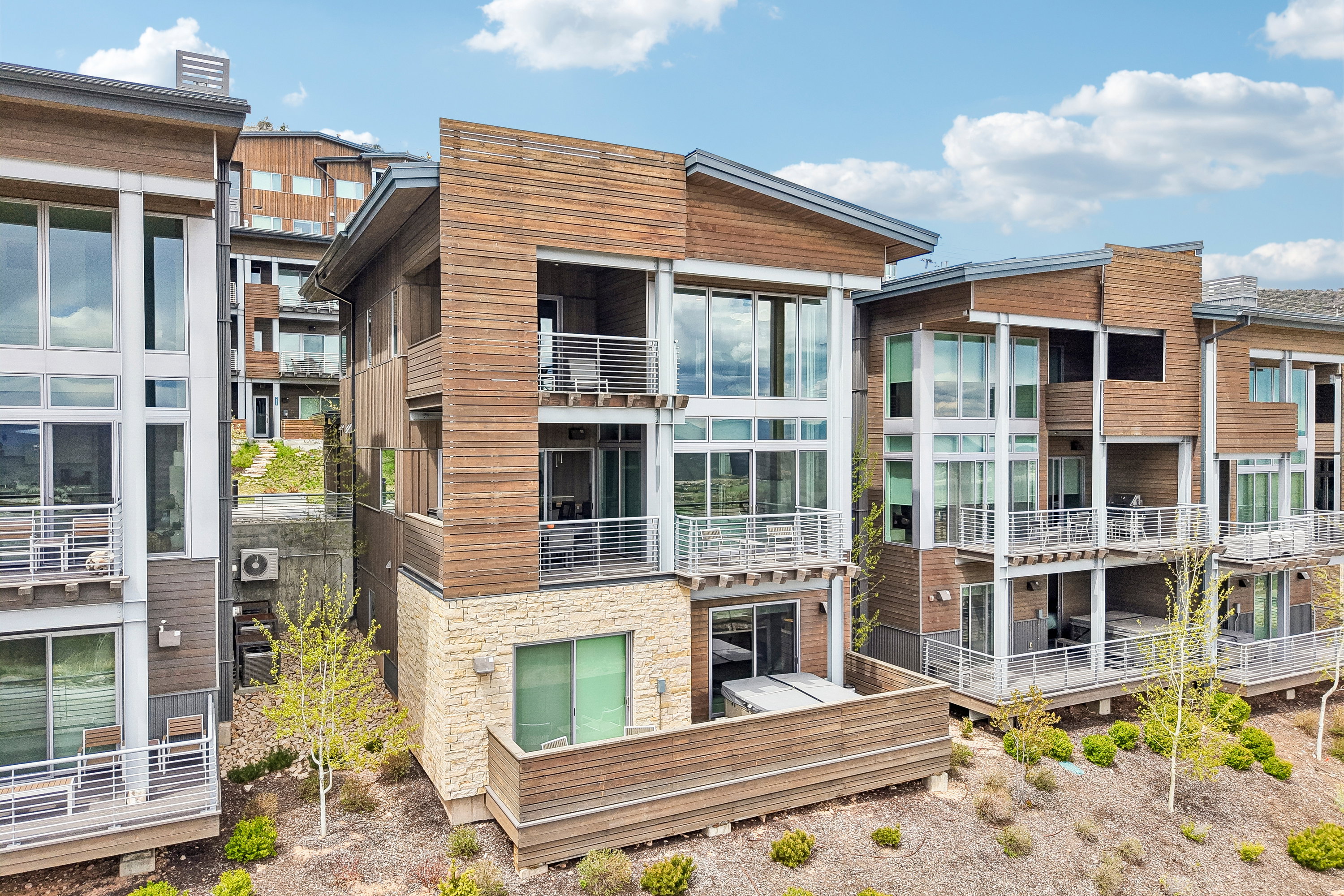 Contemporary multi-story residences featuring warm wood-finish siding, stone accents, and expansive window walls