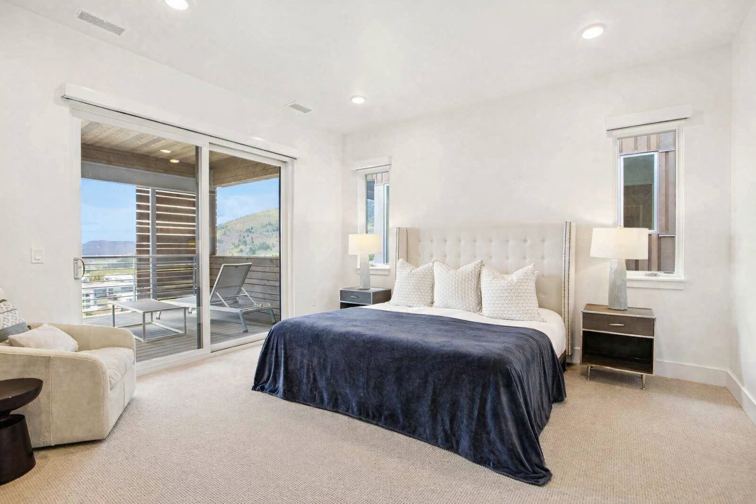 Bright bedroom featuring a private balcony with mountain scenery, recessed lighting, carpet flooring, and two side windows