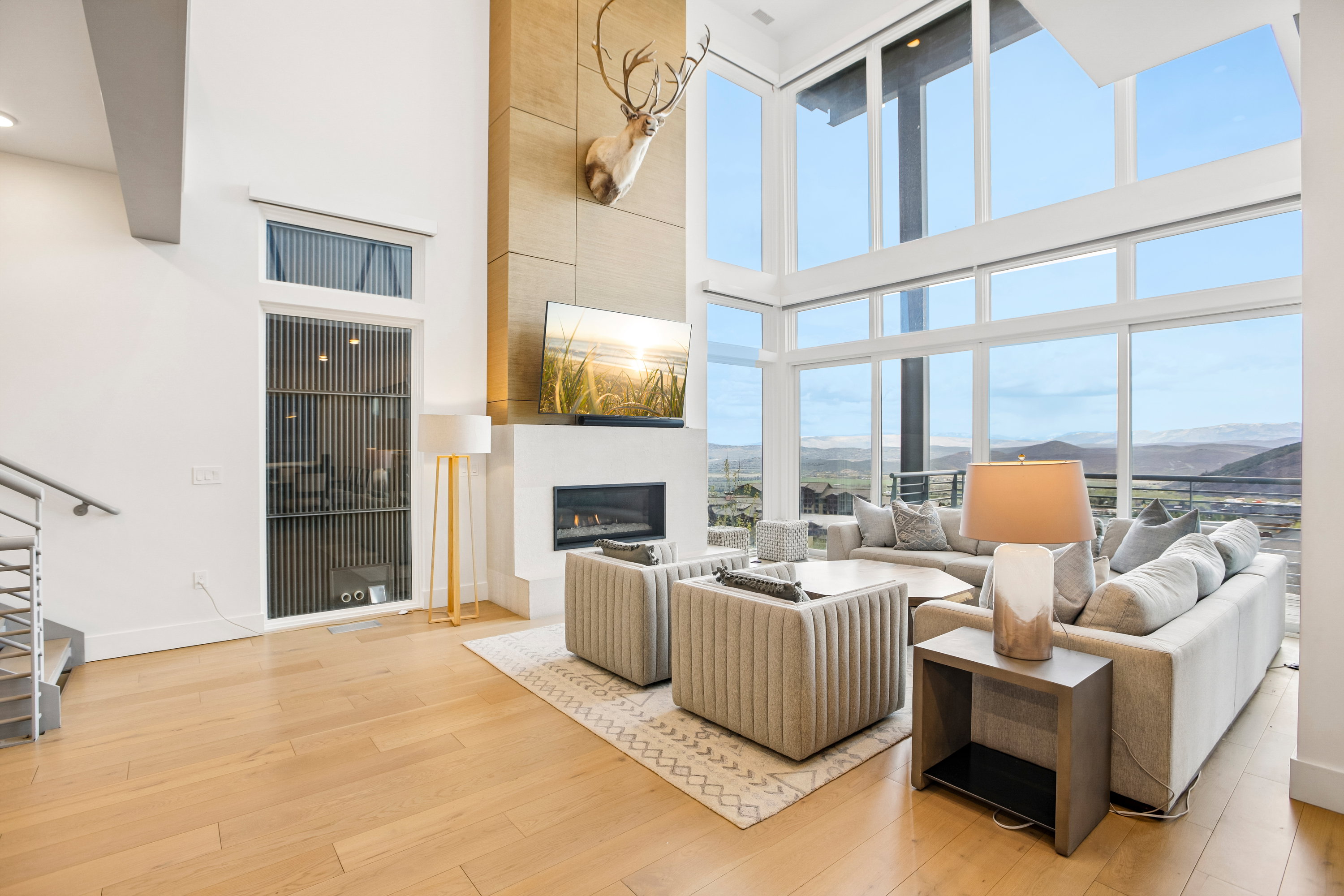 Spacious living area featuring expansive floor-to-ceiling windows, light wood-finish flooring, a contemporary fireplace with a white surround, and a striking vertical wood-paneled accent wall
