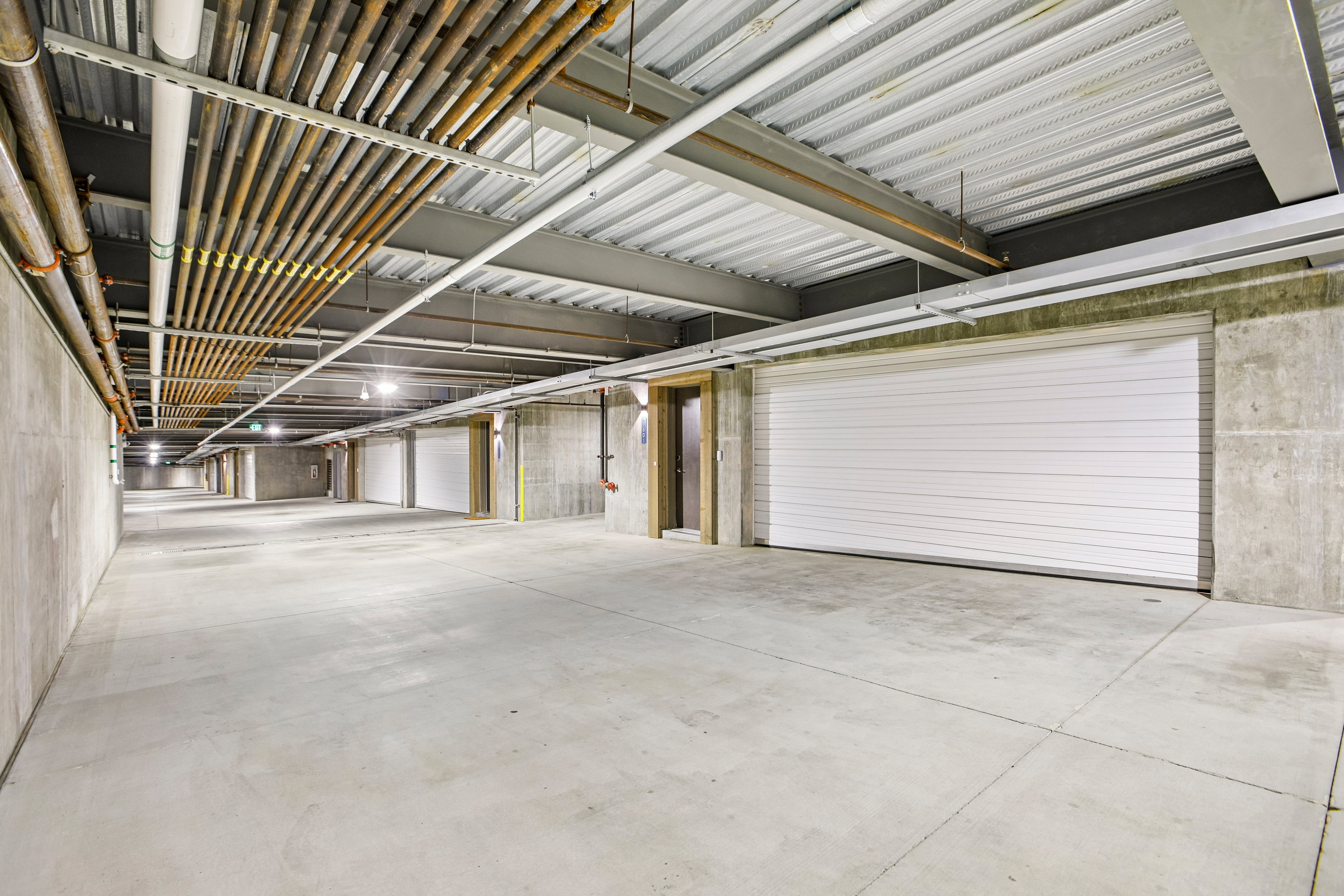 Spacious underground garage featuring concrete walls, concrete flooring, exposed ceiling utilities, roll-up garage doors, and overhead lighting