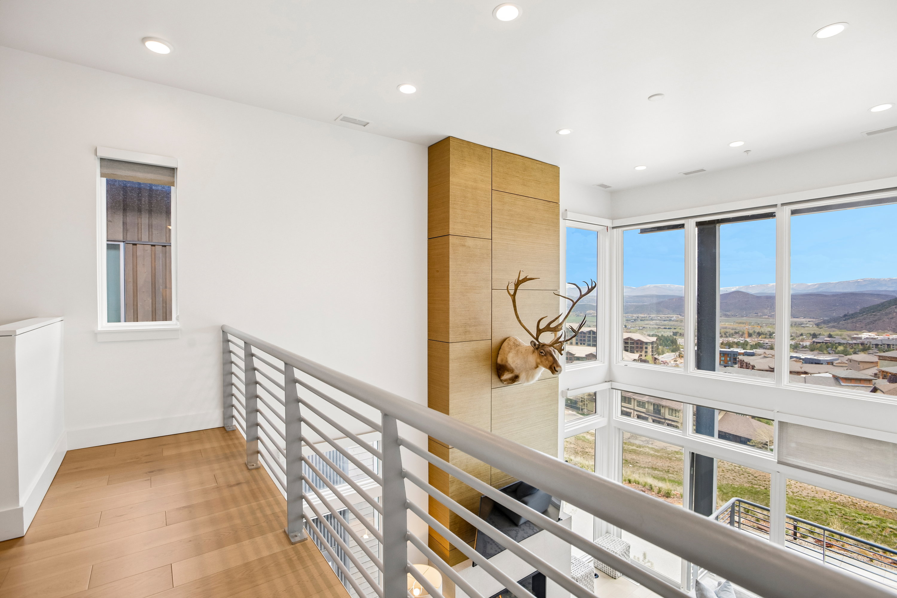 Upper-level hallway with wood-finish flooring, white walls, and recessed lighting