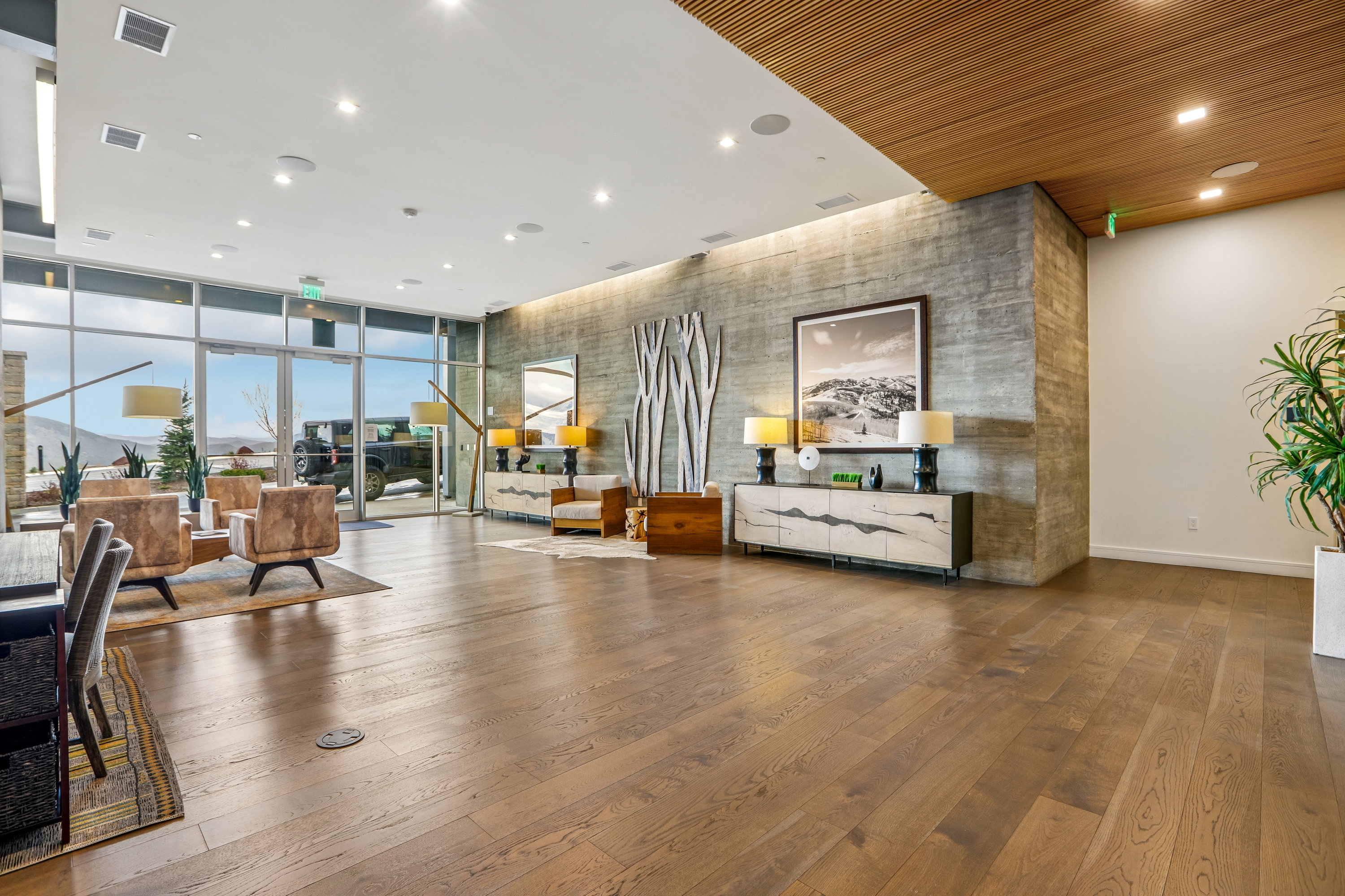 Spacious interior featuring wide plank wood-finish flooring, a full wall of floor-to-ceiling windows, and a concrete-finish accent wall