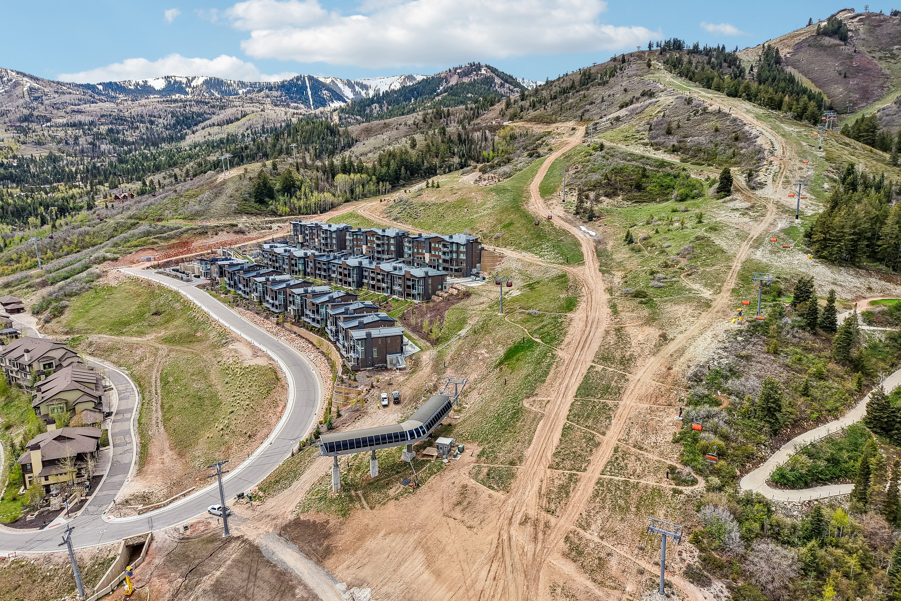 Contemporary multi-story residences featuring dark facades and flat roofs, situated on a sloped terrain with paved roads