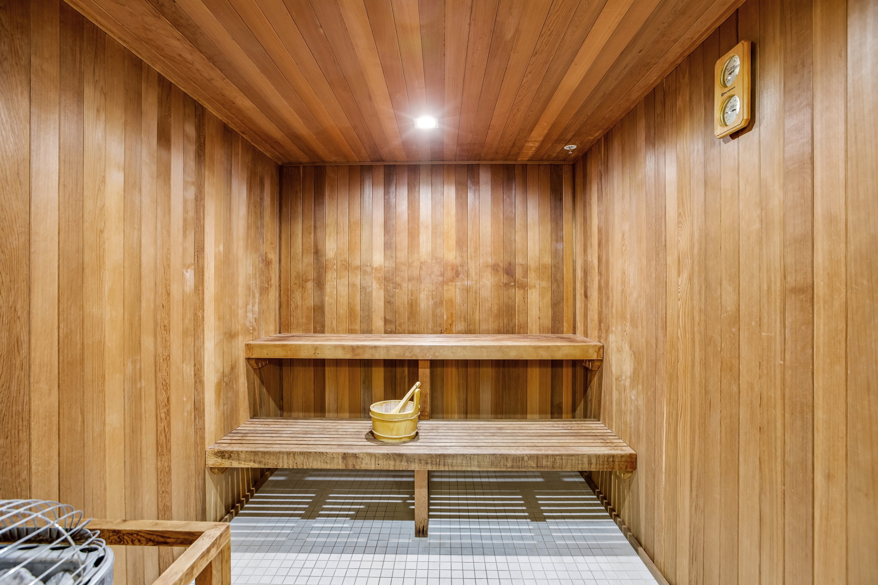 Wood-paneled sauna featuring two tiers of built-in benches, recessed ceiling lighting, and a ceramic tile floor