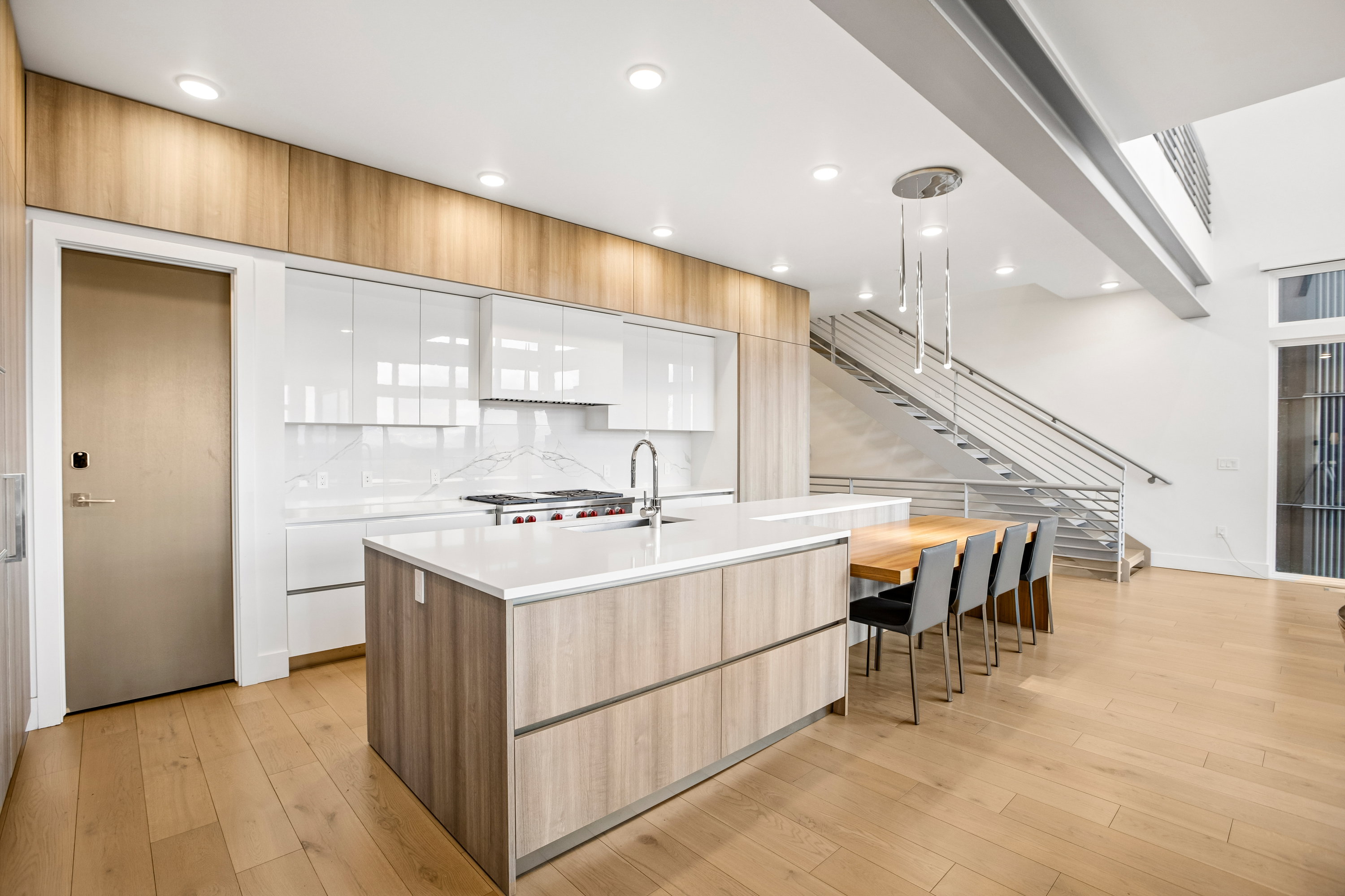 Contemporary kitchen featuring a large island with integrated dining, white cabinetry, wood-finish flooring, and a stainless steel appliance suite