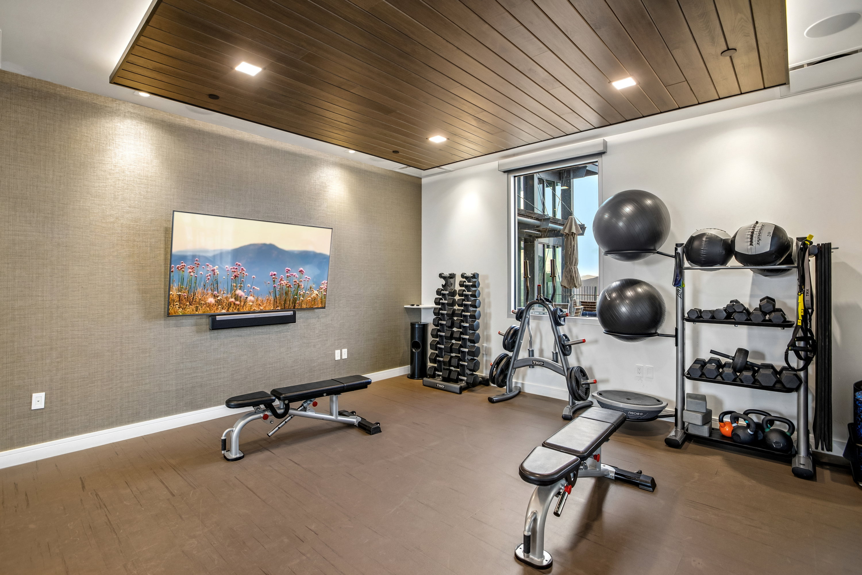 Dedicated fitness area featuring durable flooring, a textured accent wall, recessed lighting, and a wood-finish ceiling detail
