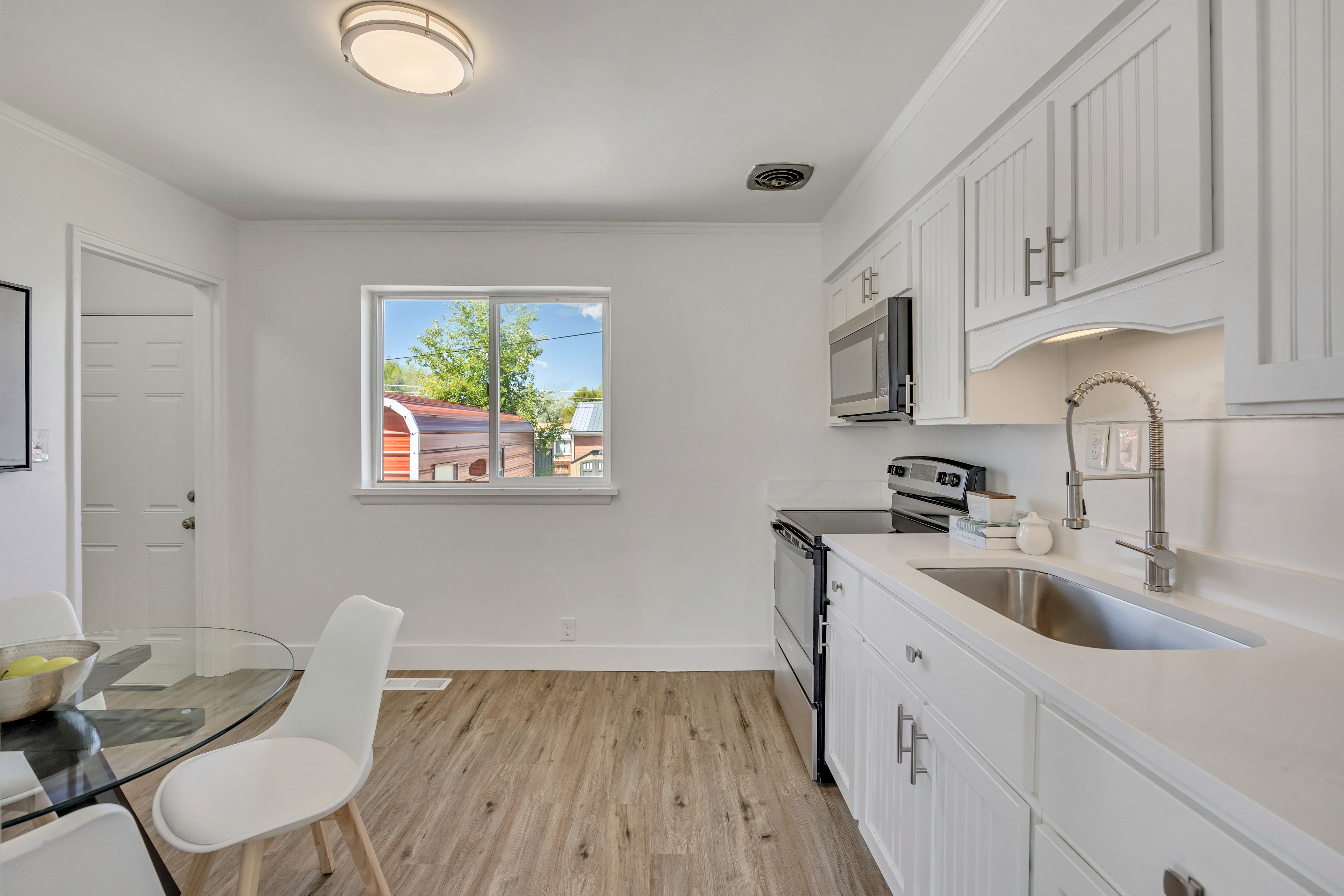 Kitchen featuring white cabinetry, stainless steel appliances, a stainless steel sink with a pull-down faucet, and wood-finish flooring
