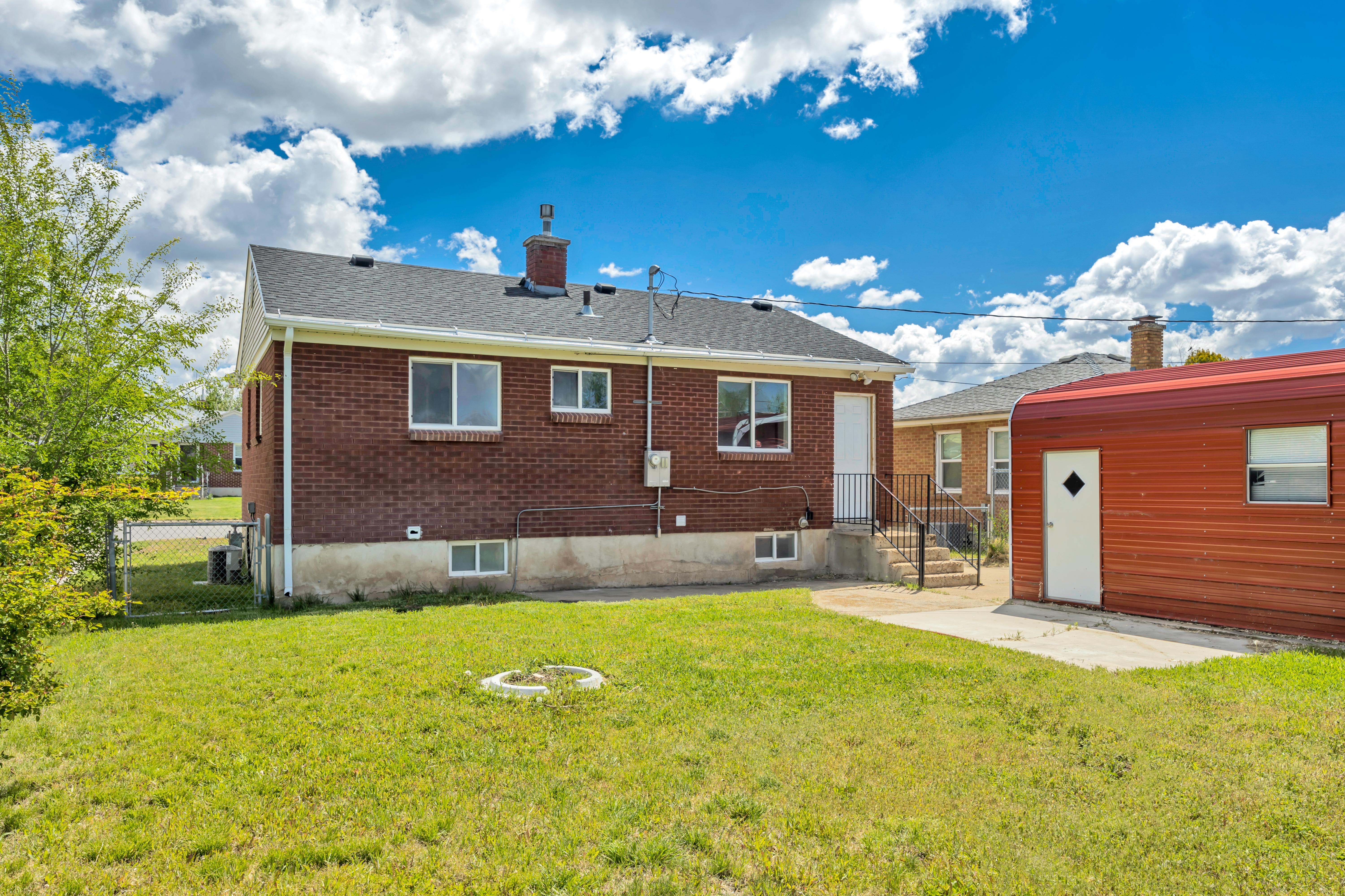 Spacious backyard featuring a chain-link fence, a separate red corrugated metal outbuilding with a white entry door, and a concrete pad
