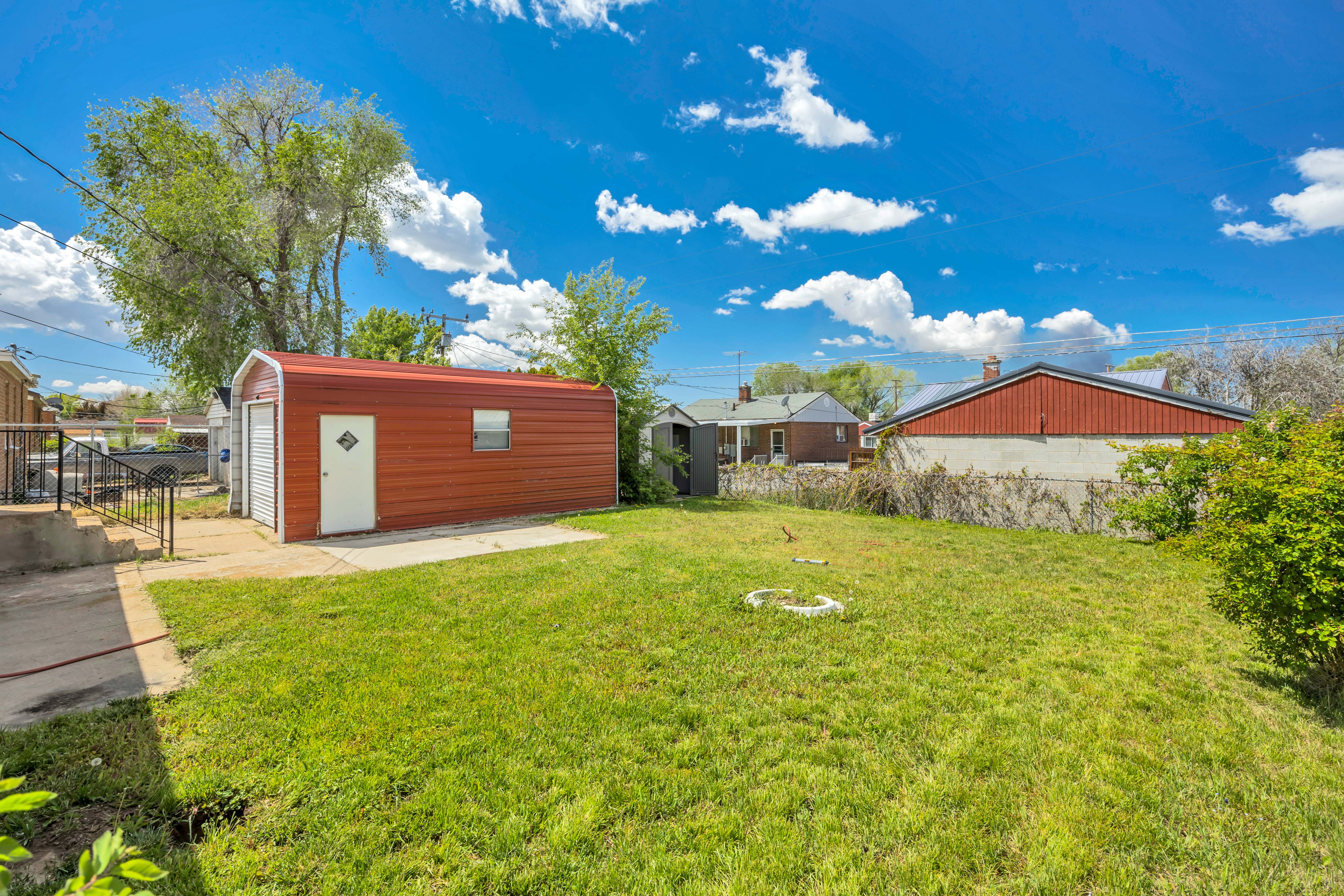Expansive green lawn with a detached red metal garage featuring a roll-up door and a separate side entry